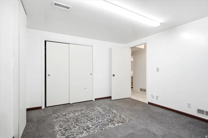 Carpeted room with white walls, featuring sliding closet doors and a wall-mounted fluorescent light fixture