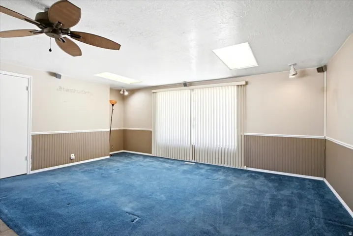 Spacious room featuring a ceiling fan, two skylights, and vertical blinds over a large window