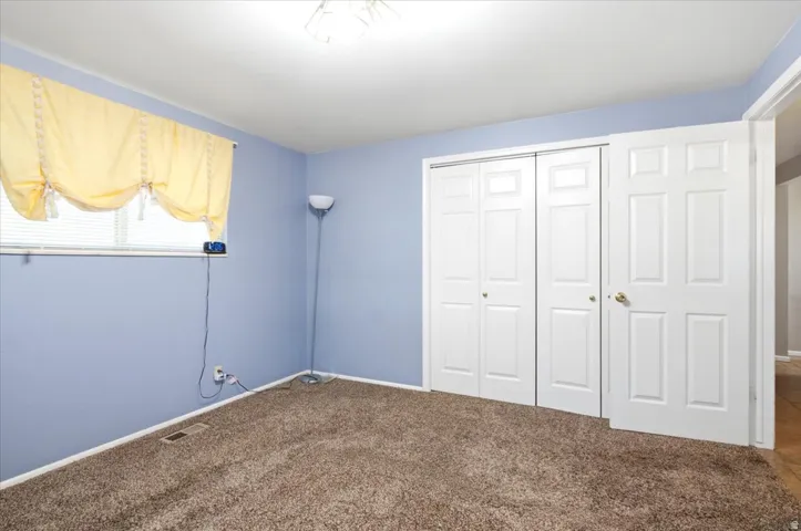 Plush brown carpeting throughout, complemented by a window with horizontal blinds and a ceiling-mounted light fixture