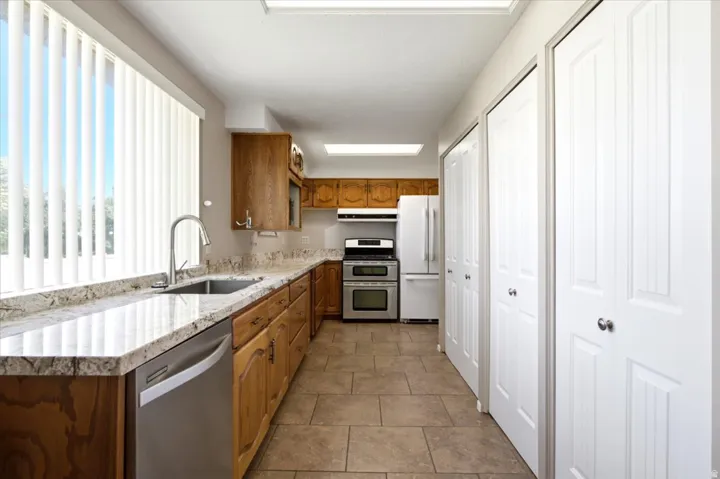 Galley kitchen featuring light-toned wood cabinetry, granite countertops, and tile flooring