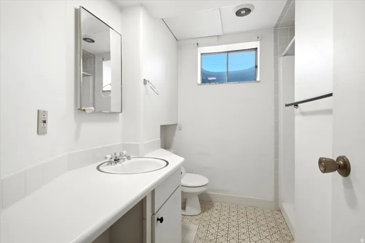 Bathroom featuring a vanity with an integrated sink, patterned tile flooring, a mirrored medicine cabinet, and a window