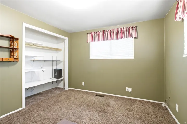 Spacious room featuring neutral carpeting, a window with blinds, and an organized closet with shelving and a hanging rod