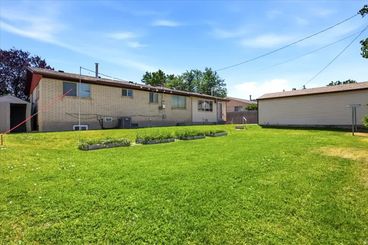 Expansive grassy yard area featuring raised garden beds, a storage shed, and a brick exterior building