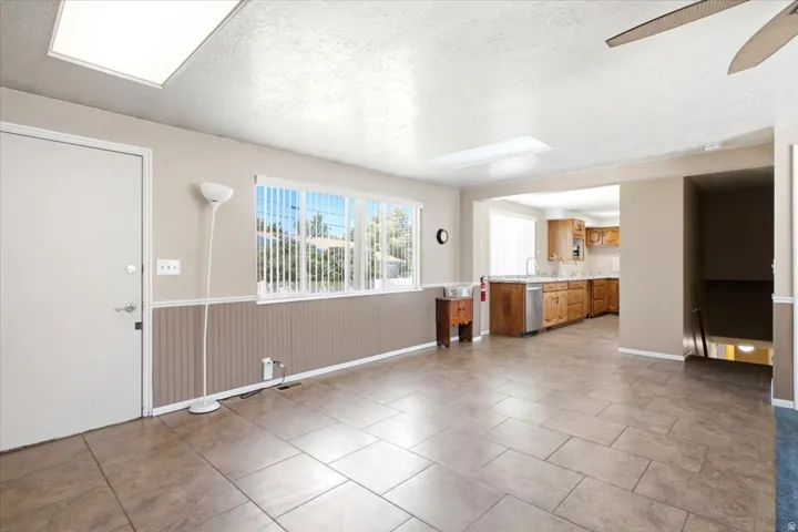 Spacious living area featuring tile flooring, a large window with vertical blinds, and a skylight