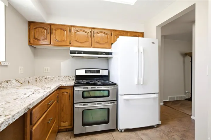 Kitchen featuring wood cabinetry, light-toned stone countertops, and a stainless steel double oven range with a coordinating vent hood