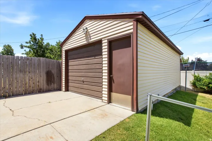 Detached garage featuring horizontal siding, a brown sectional garage door, a side entry door, and a concrete driveway