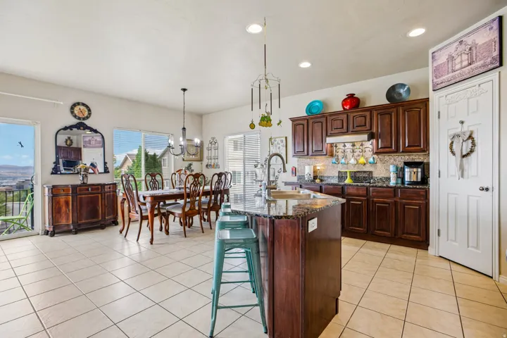 Open-concept kitchen and dining area featuring tile flooring, a kitchen island with a built-in sink, dark wood cabinetry, and a full-size dining table with seating