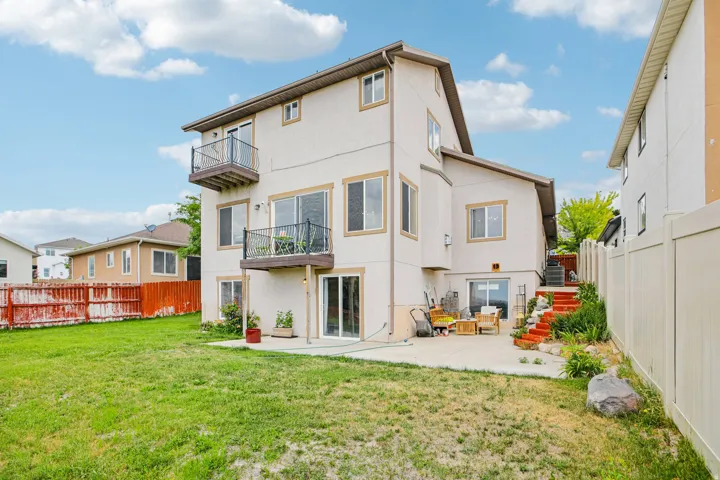 Rear exterior with two balconies featuring black wrought iron railings, a ground-level patio, and a walk-out basement