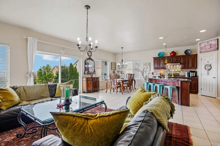 Open-concept living space featuring light-toned tile flooring, large sliding glass doors, a kitchen island with seating, dark wood cabinetry, and recessed lighting