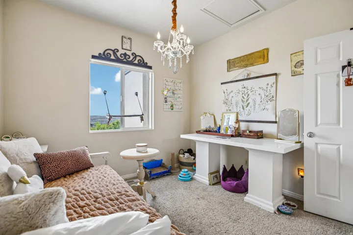 Bright room with a window featuring an ornate decorative valance, a built-in white desk, a crystal-style chandelier, a white paneled door, and neutral-toned carpeting