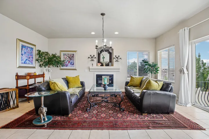 Spacious living area featuring a fireplace with mantle, tile flooring, two windows with blinds, and a sliding glass door opening to a balcony