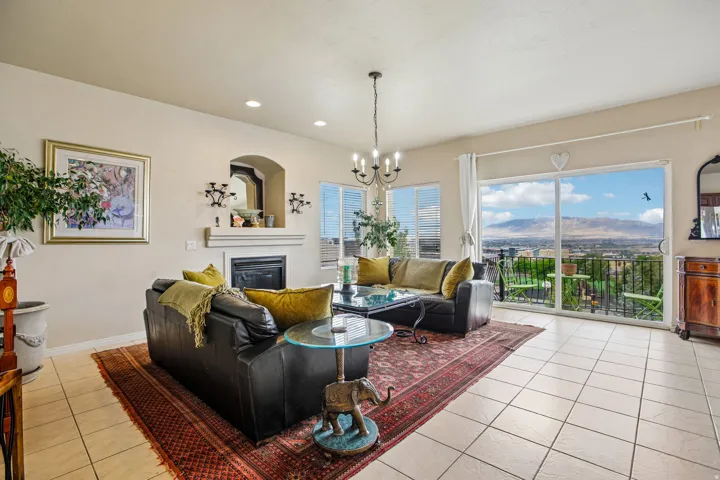 Spacious living area featuring neutral-toned walls, tile flooring, a fireplace with a mantel and arched niche, and a glass sliding door opening to a balcony with mountain scenery