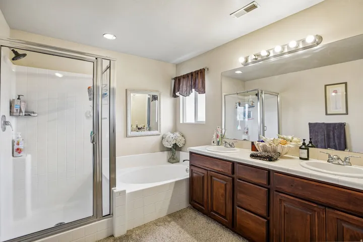 Bathroom featuring a glass-enclosed shower, a separate built-in soaking tub, and a dual-sink vanity with wood cabinetry