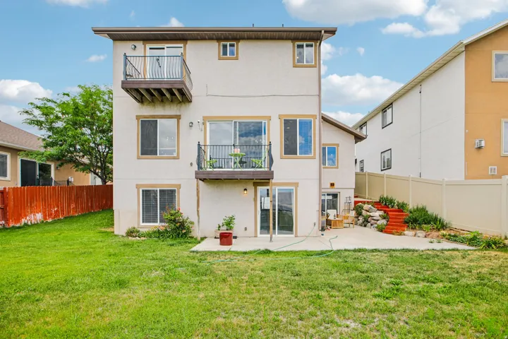 Rear exterior featuring two balconies with metal railings, a concrete patio, and a grass lawn