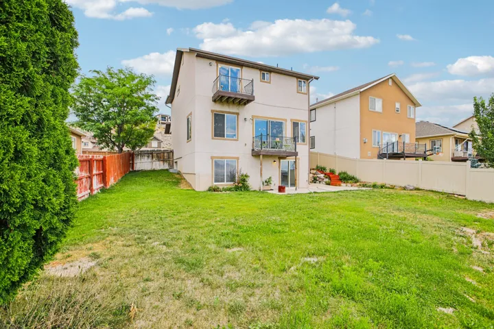 Expansive backyard featuring a stucco exterior, upper-level balcony, lower-level patio access, and a partial privacy fence