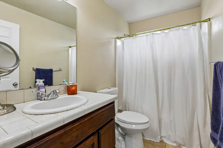 Bathroom featuring a wood-finish vanity with a tile countertop, integrated sink, and wall-mounted mirror