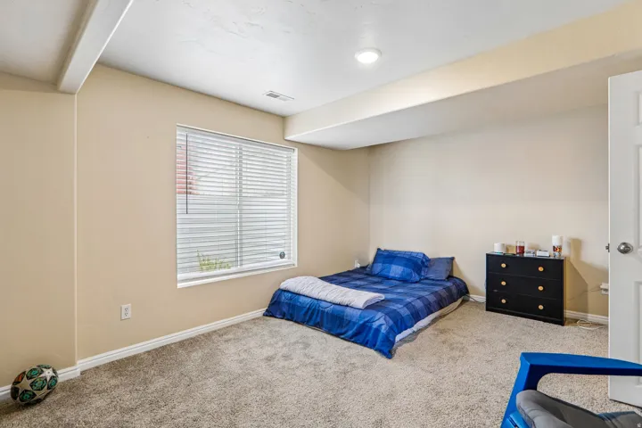 Spacious room featuring neutral-toned walls, plush carpet flooring, a large window with blinds, and white trim throughout