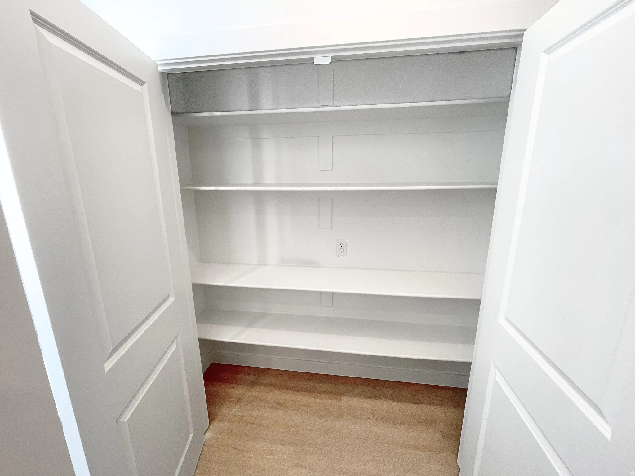 White bi-fold doors open to a pantry featuring five built-in white shelves and wood-finish flooring