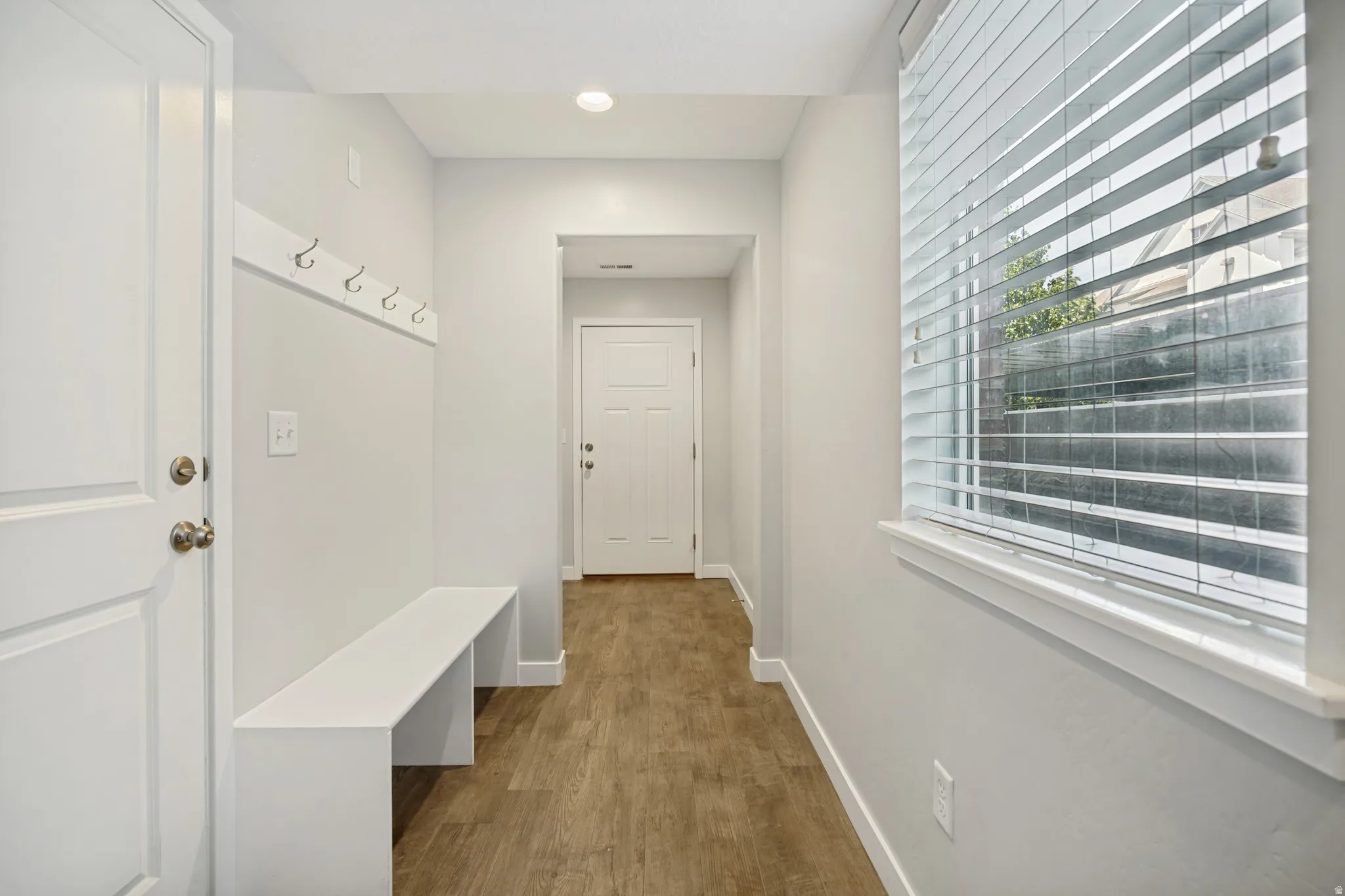 A thoughtfully designed entryway showcasing laminate flooring, a built-in bench, coat hooks, and natural light.