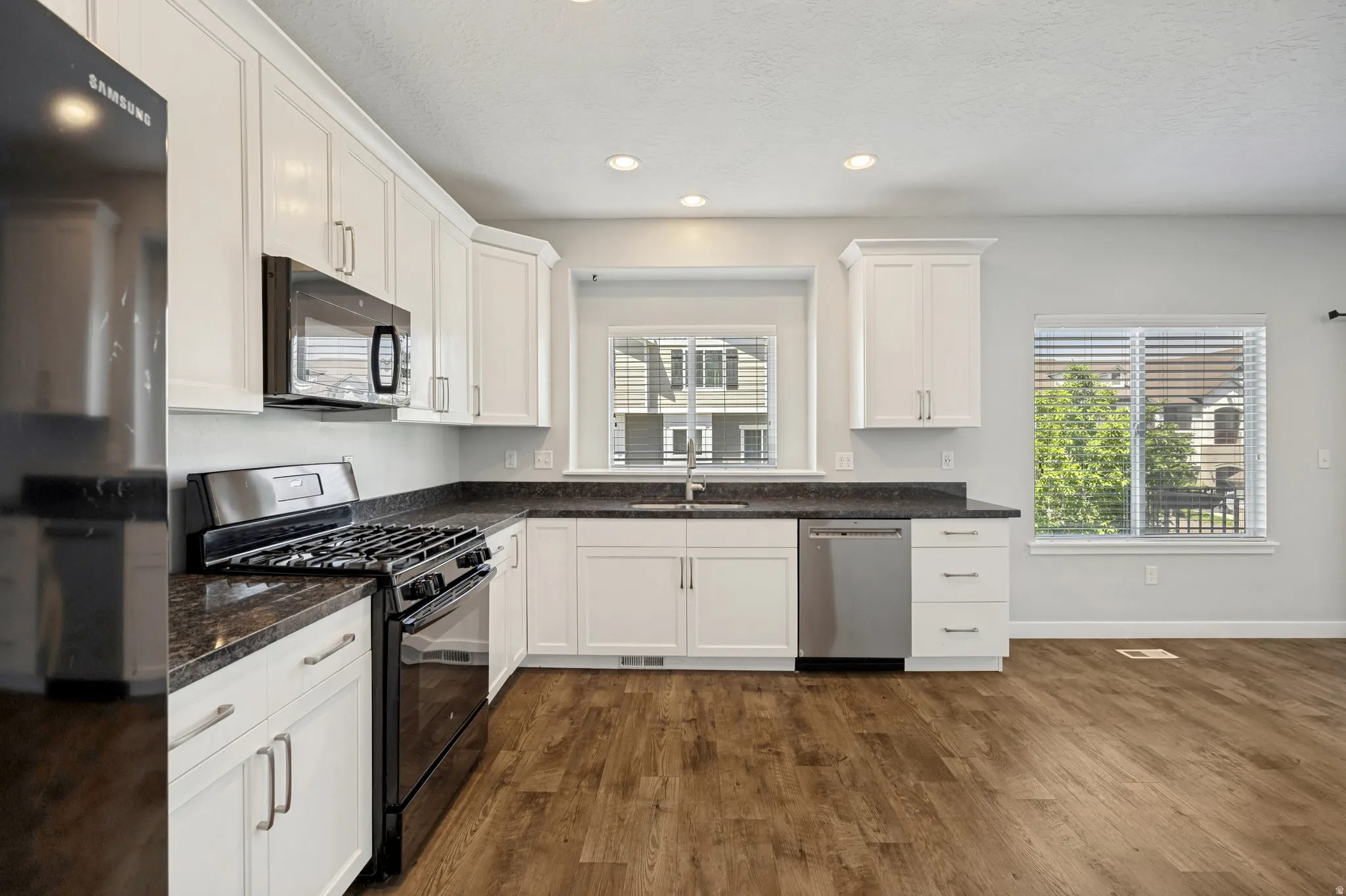 Kitchen featuring white shaker-style cabinetry, dark granite-look countertops, stainless-steel dishwasher, black gas range, and recessed lighting