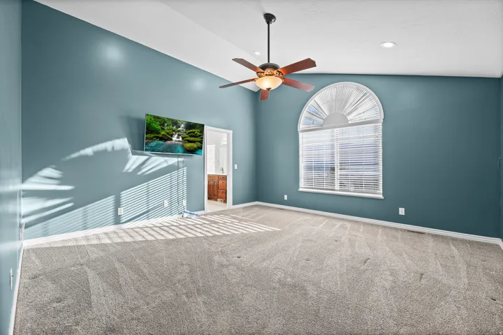Spacious room featuring vaulted ceilings, a ceiling fan with integrated lighting, recessed lighting, an arched window with blinds, and neutral-toned carpeting