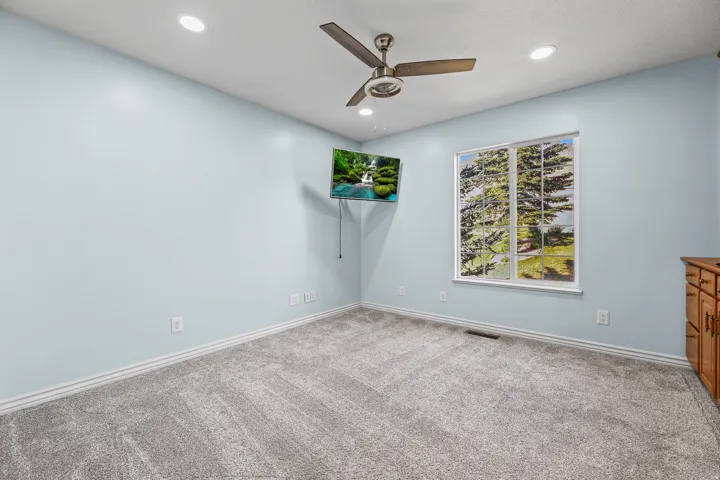 Light blue interior wall paint, recessed ceiling lighting, a ceiling fan, a window, and wood cabinetry
