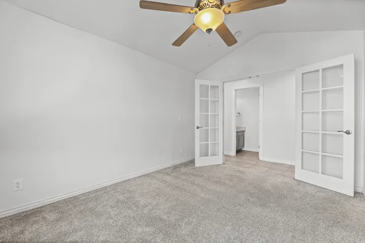 Carpeted room featuring a ceiling fan with integrated lighting, vaulted ceiling, and French doors