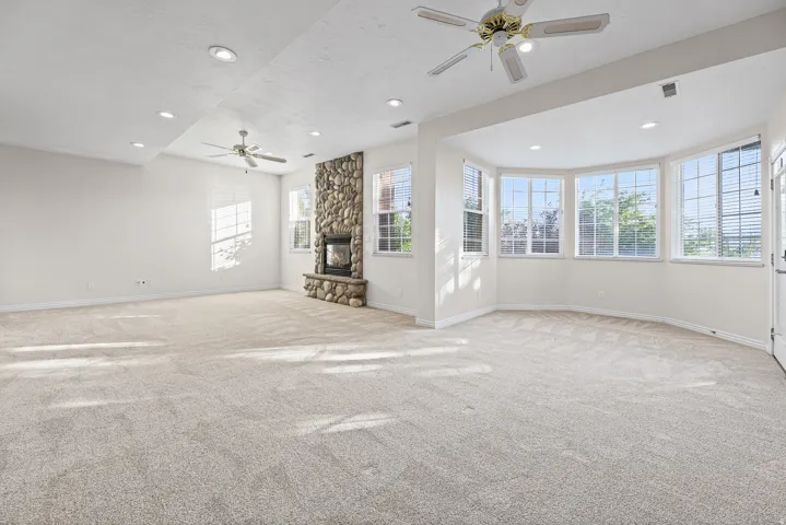 Spacious room featuring a floor-to-ceiling river stone fireplace, bay windows, recessed lighting, and ceiling fans