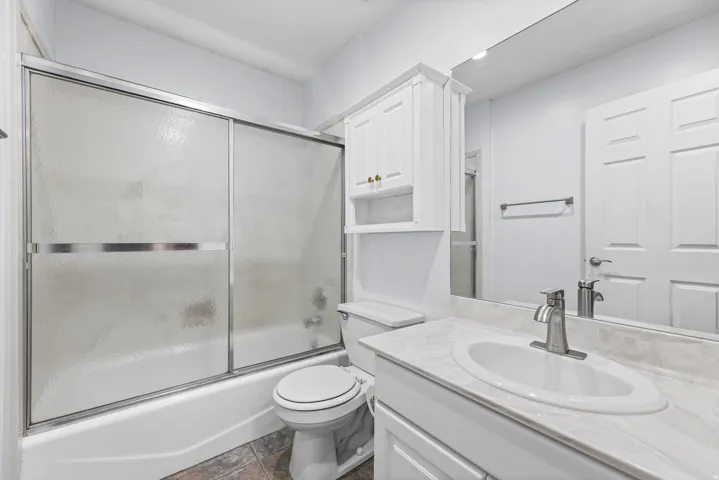 Bathroom featuring a full-size tub with sliding frosted glass doors, a vanity with an integrated sink and light-toned countertop, a wall-mounted medicine cabinet with gold-toned hardware, and mosaic-style floor tiling