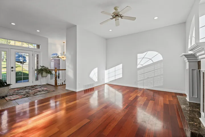 Expansive living area featuring polished wood-finish flooring, a decorative fireplace with a marble-finish hearth, a ceiling fan, and recessed lighting
