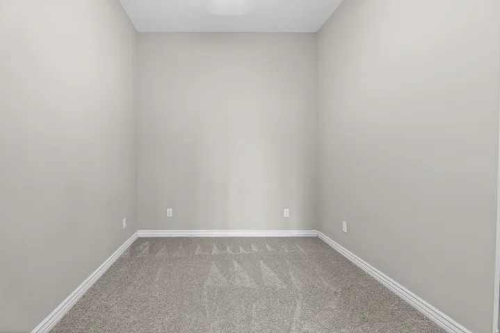 Room featuring neutral-toned walls, gray patterned carpeting, white baseboards, and a ceiling light fixture