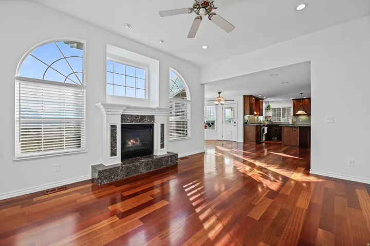 Hardwood flooring throughout a bright living space featuring a fireplace with a stone surround and hearth, framed by arched and rectangular windows