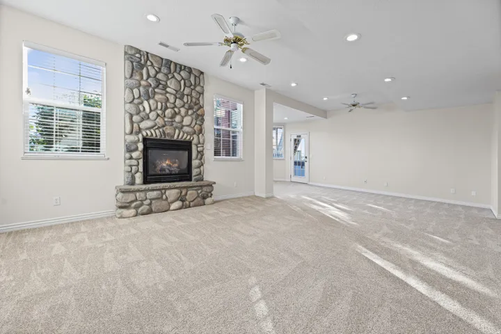 Spacious living area featuring a floor-to-ceiling stone fireplace, plush carpeting, recessed lighting, and multiple windows with blinds