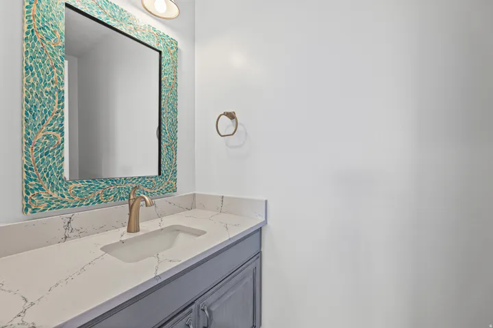 Vanity featuring a patterned mirror, single basin sink, and brass-finish faucet