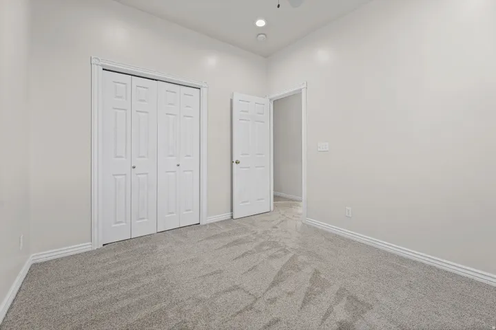 Neutral-toned room featuring a patterned grey carpet, white baseboards, and a white bi-fold closet door