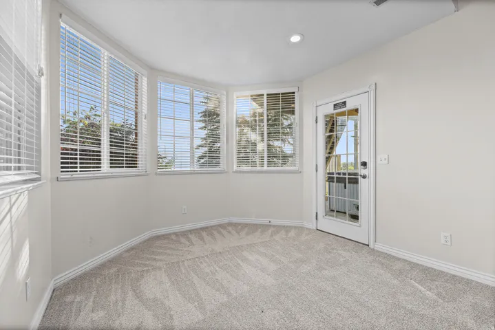 Carpeted room with a bay window design featuring multiple windows with blinds, a recessed ceiling light, and a white door with glass panels