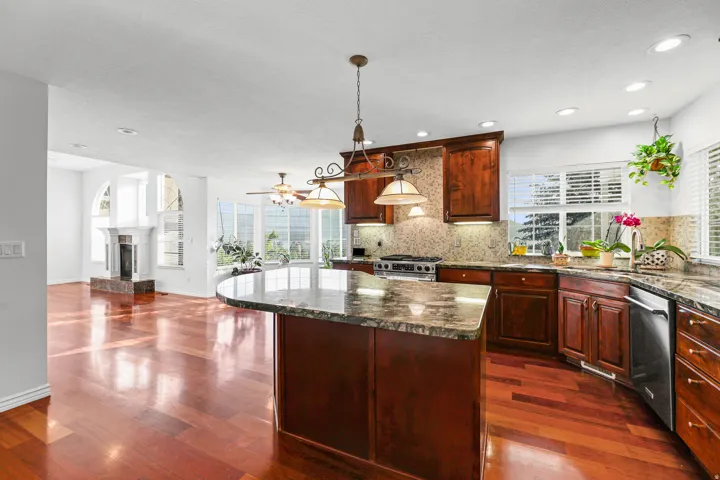 Spacious kitchen featuring an expansive island with a stone countertop, rich wood cabinetry, stainless steel appliances, and wood-finish flooring throughout