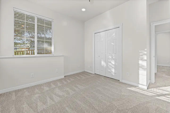 Carpeted room featuring a window with horizontal blinds, bi-fold closet doors, recessed ceiling lighting, and crisp white trim