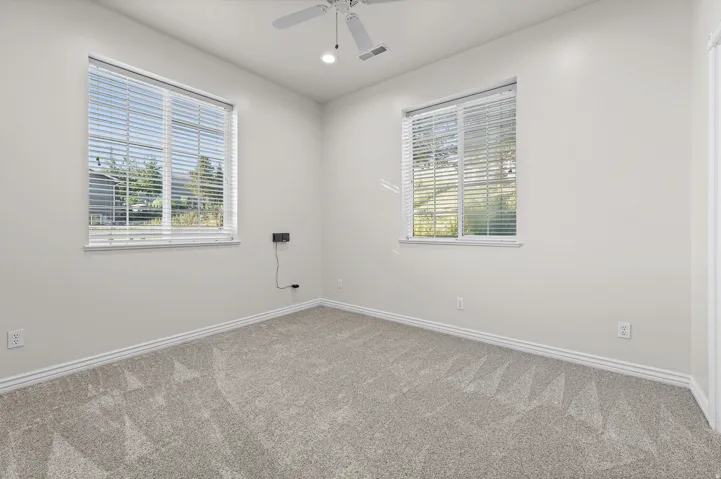 Room featuring neutral wall tones, two windows with blinds, a ceiling fan with integrated lighting, and light-toned carpeting