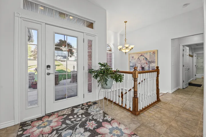 Entryway featuring double glass-panel doors with sidelights and a transom window, a tiled floor, and a staircase with a wood handrail and white balusters