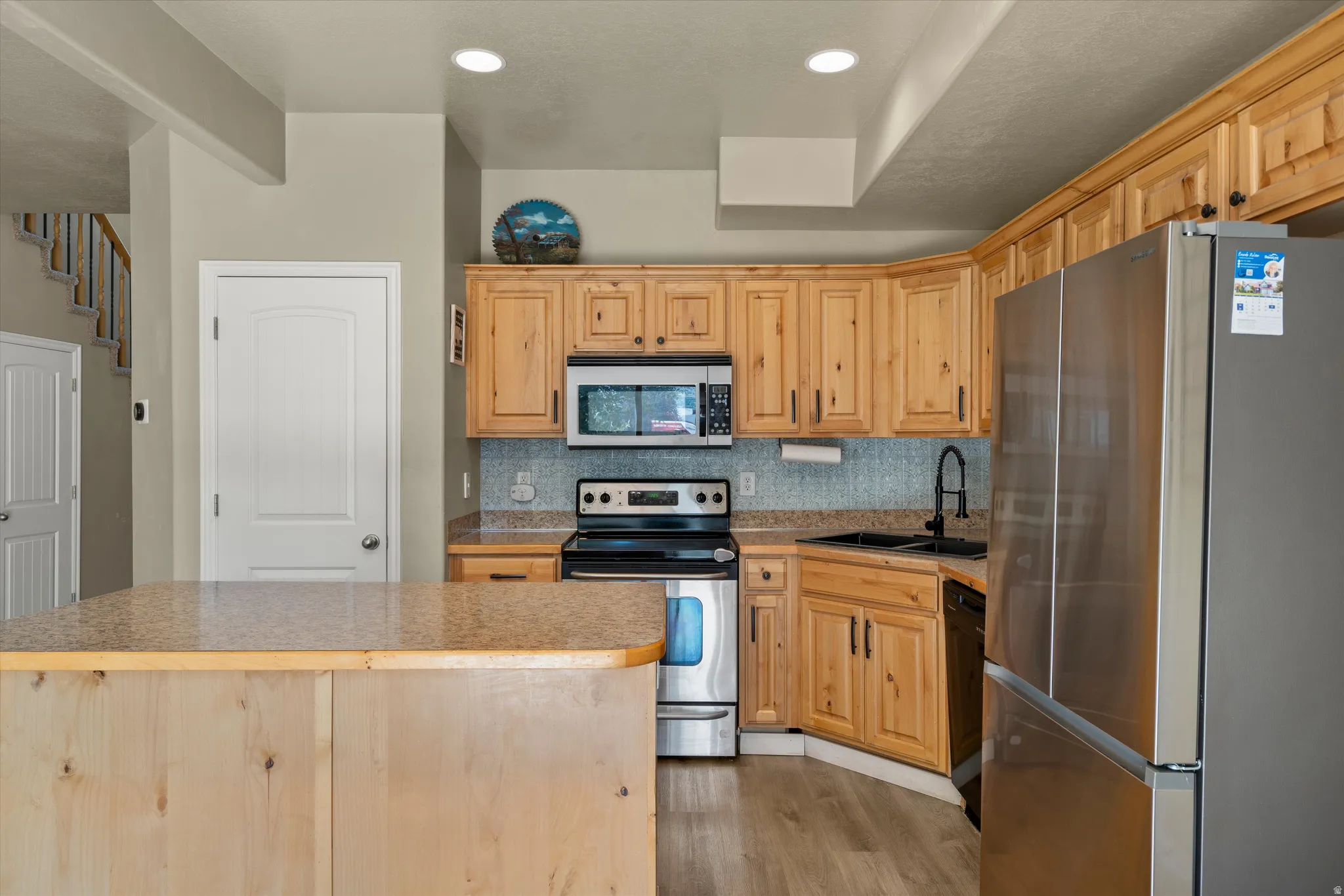 Kitchen featuring wood-finish cabinetry, stainless steel appliances, granite-style countertops, mosaic tile backsplash, and a central island with a matching granite-style surface