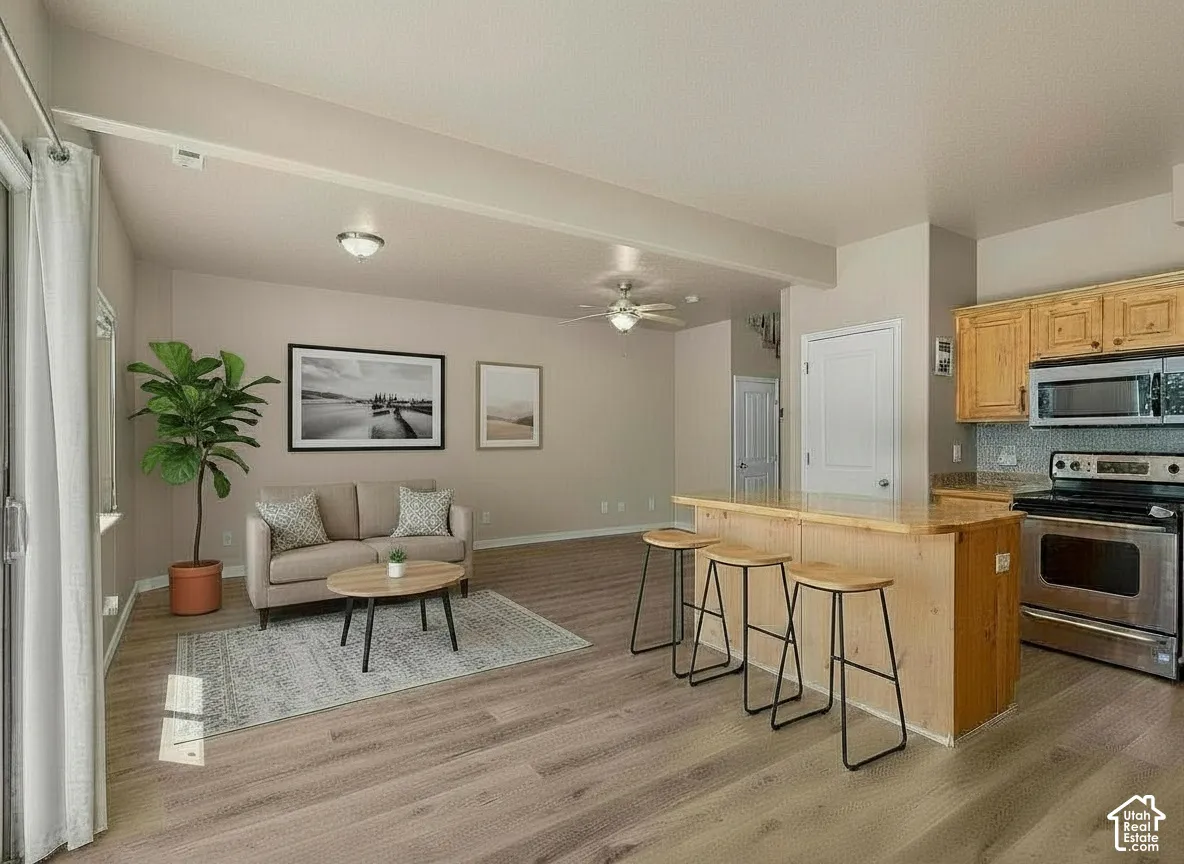 Open concept floorplan featuring wood-finish flooring, kitchen island with seating, stainless steel appliances, and a glass sliding door