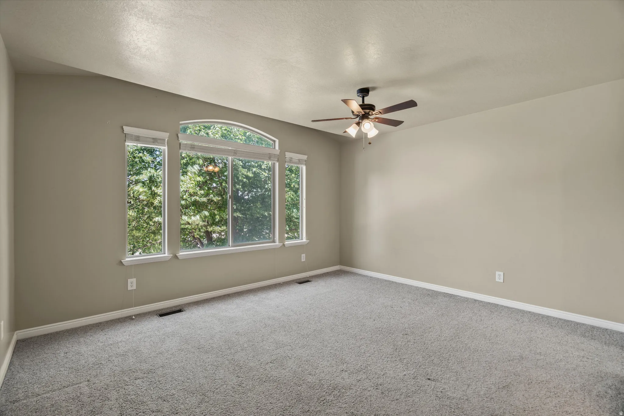 Spacious room featuring a multi-pane window with an arched transom, a ceiling fan with integrated lighting, and neutral wall paint