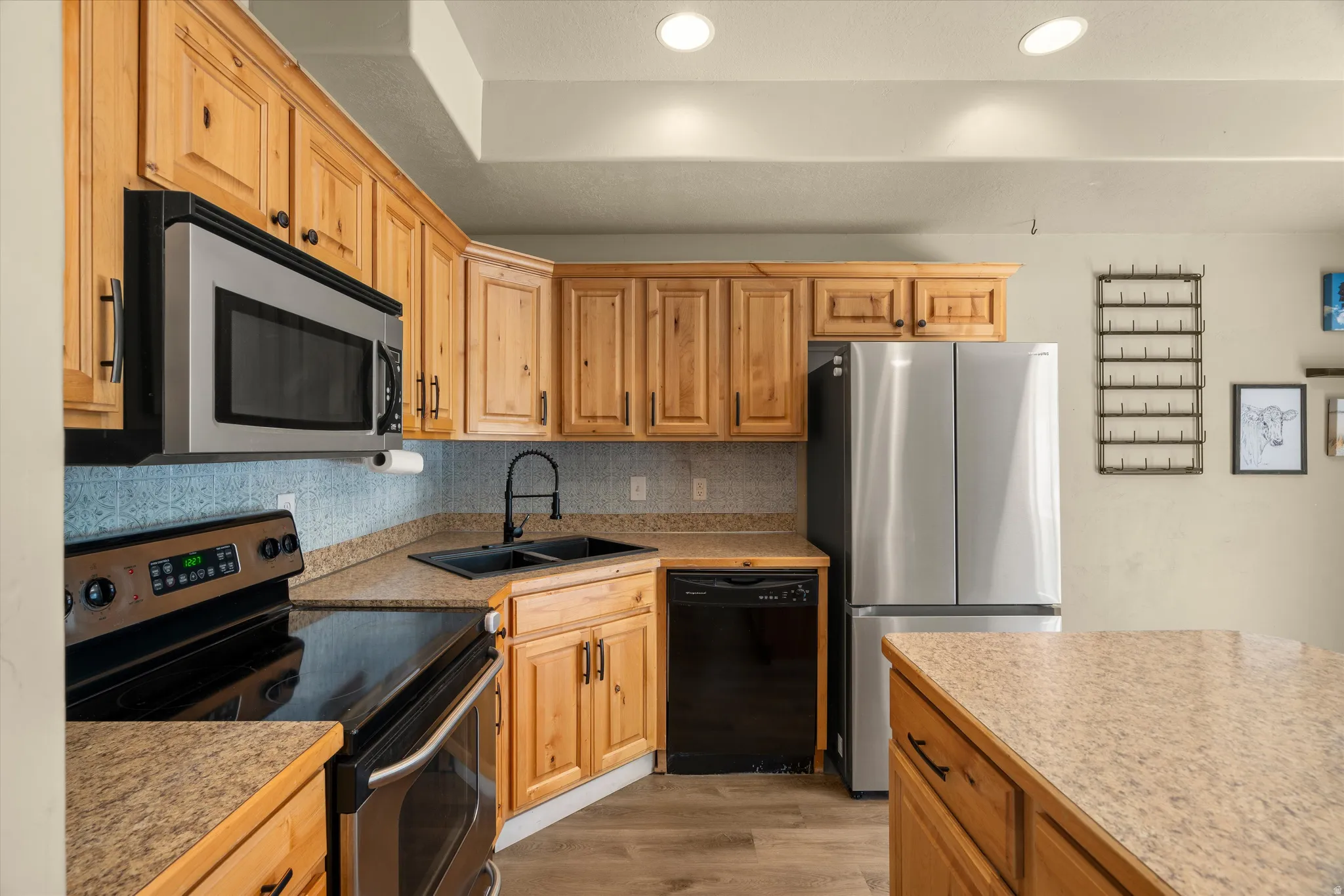 Kitchen featuring wood cabinetry, stainless steel appliances, speckled countertops, a black double basin sink with a matte black faucet, and recessed lighting