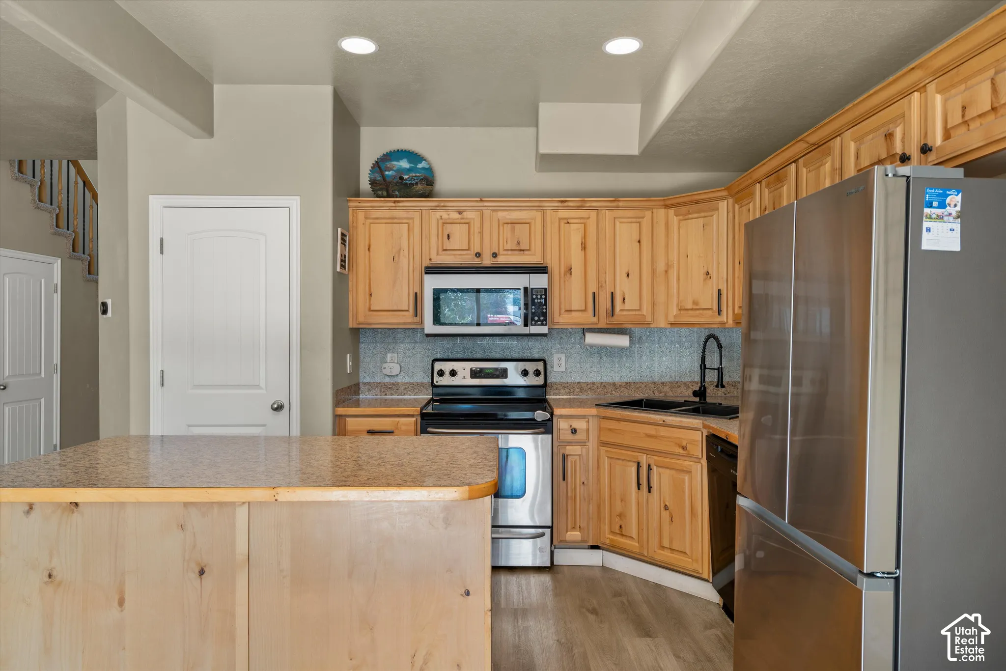 Kitchen featuring wood-finish cabinetry, stainless steel appliances, granite-style countertops, mosaic tile backsplash, and a central island with a matching granite-style surface