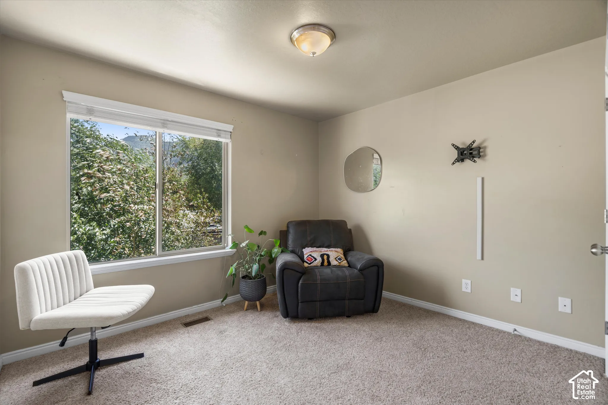 Bright room featuring a large window with white trim, tan painted walls, and light-colored carpet flooring