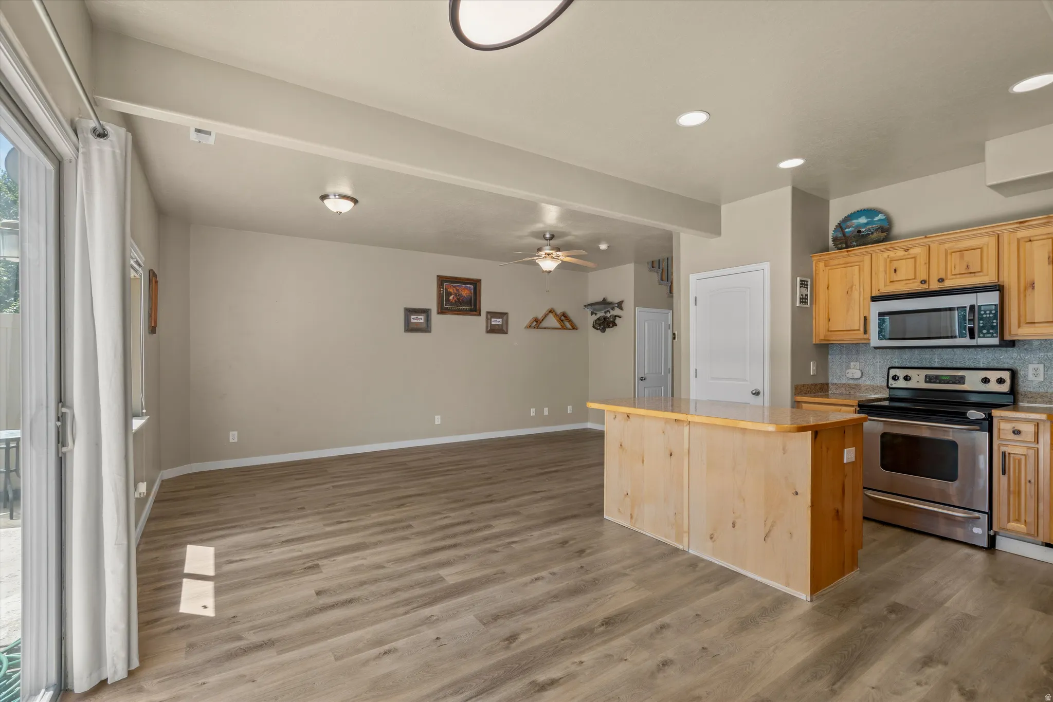 Open-concept living space featuring wood-finish flooring, a kitchen island with countertop, and stainless steel appliances including a range and microwave