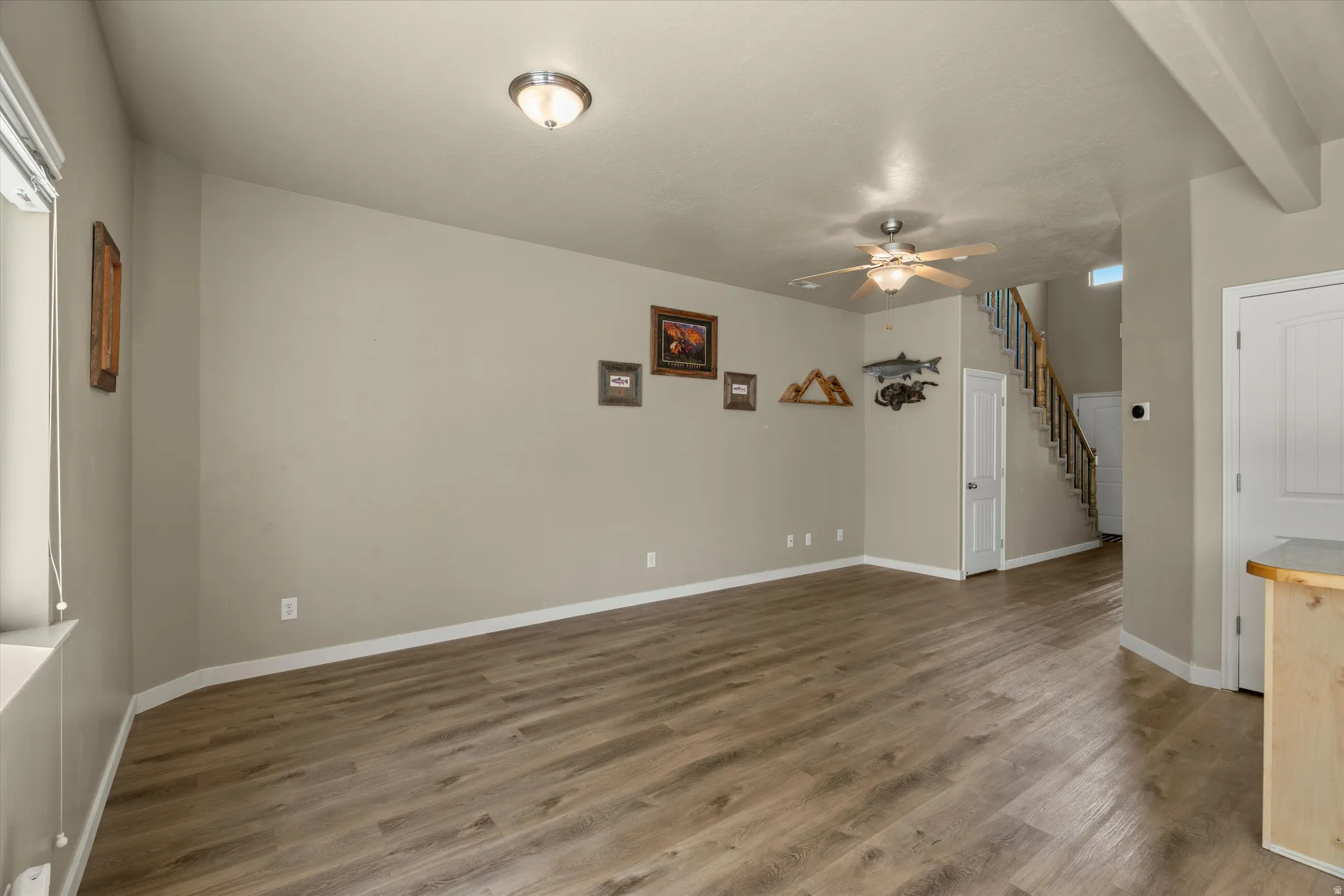 Spacious living area featuring wood-finish flooring, neutral wall tones, a ceiling fan, and a prominent staircase with wood railings