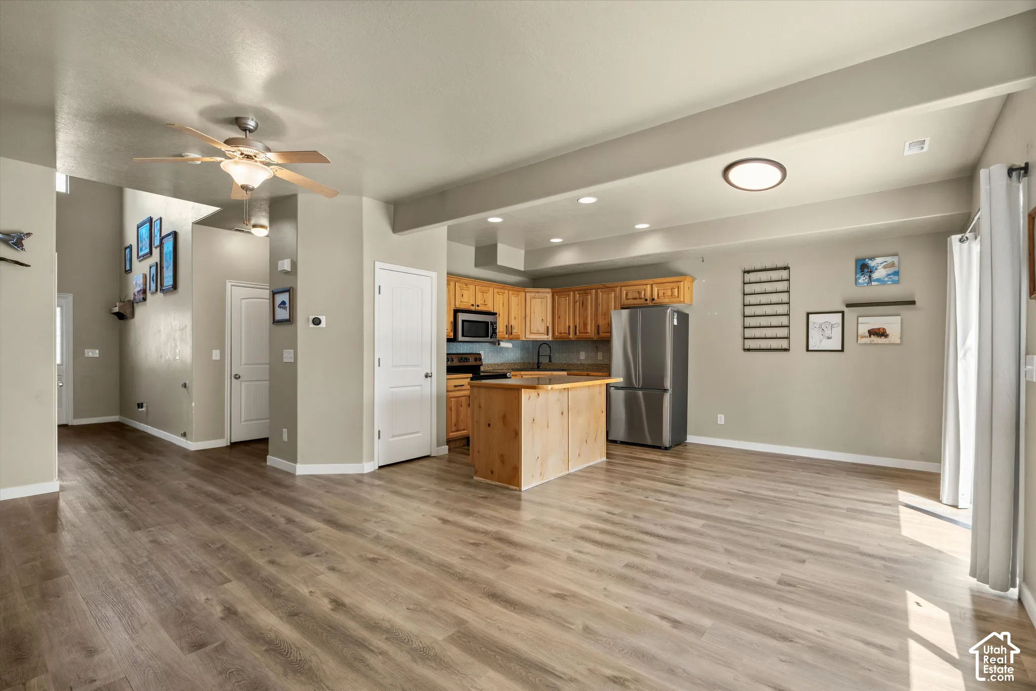 Open-concept living area with wood-finish flooring, a kitchen island, recessed lighting, and a stainless steel refrigerator