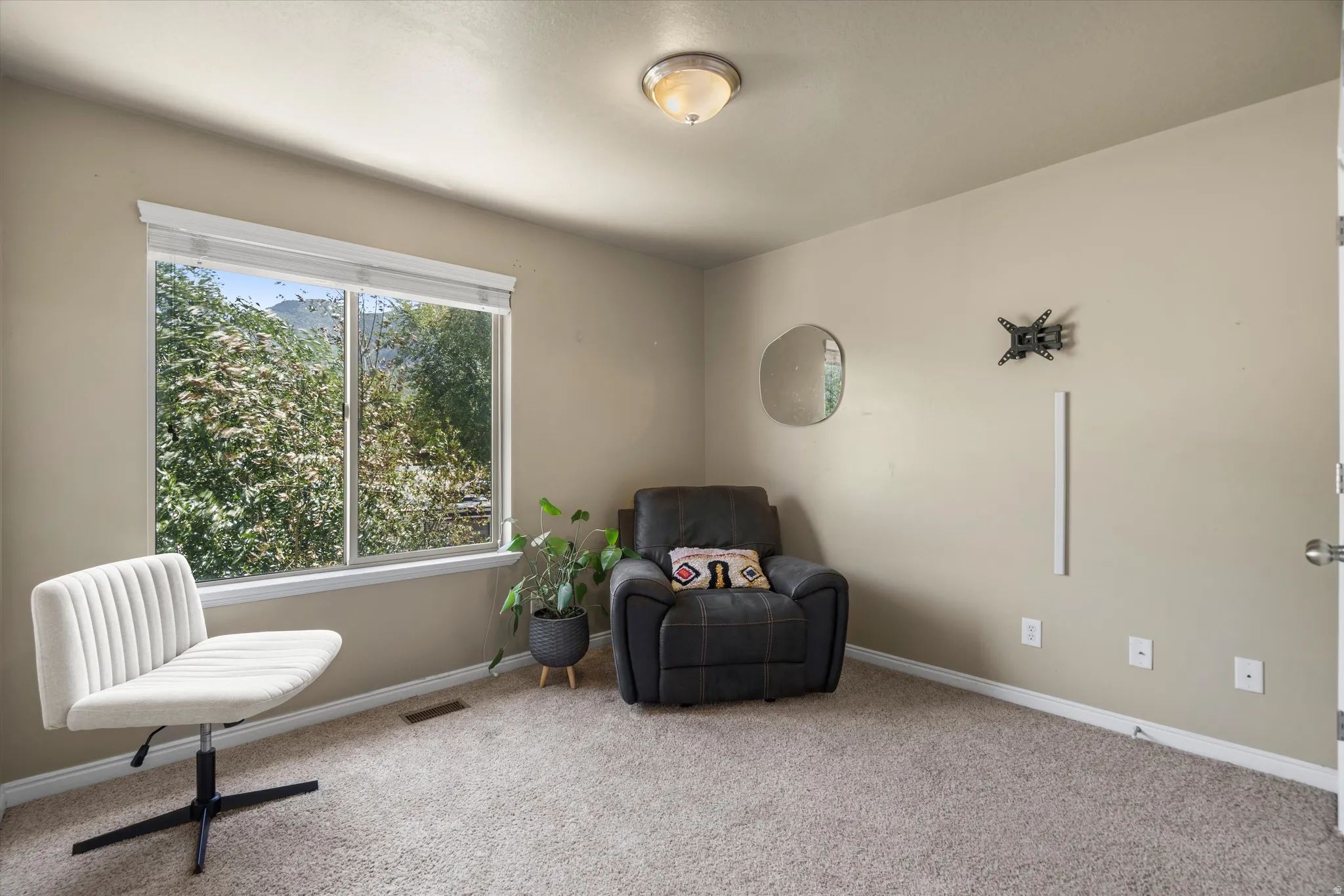 Bright room featuring a large window with white trim, tan painted walls, and light-colored carpet flooring